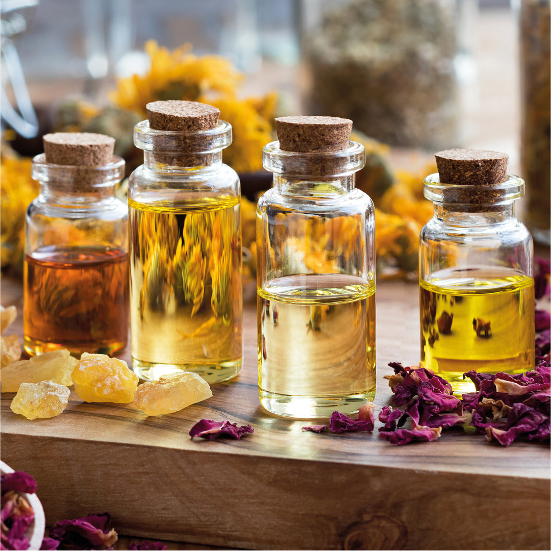 quattro barattoli contenenti olii vegetali appoggiati su un tavolo cosparso di petali e fiori 